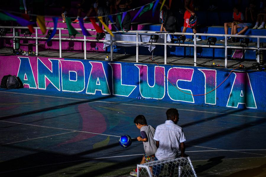 Un partido de noche en una cancha de barrio con el nombre pintado en la pared