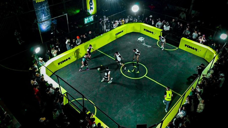 La cancha de Toma El Juego vista desde arriba, iluminada de verde y rodeada de público pegado a las vallas