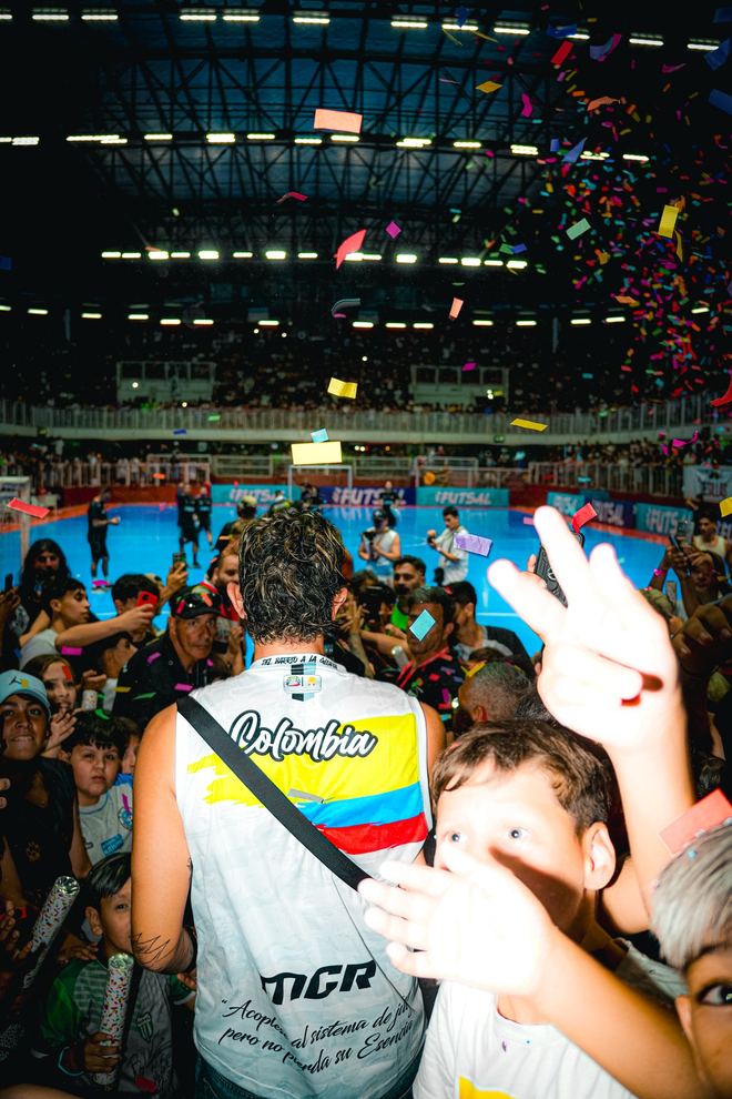 Un hincha con la banda de Colombia levanta el brazo entre la tribuna llena, con papelitos cayendo