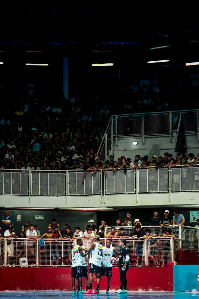 La tribuna repleta del Coliseo Malvinas Argentinas sobre la cancha azul, vista desde el fondo
