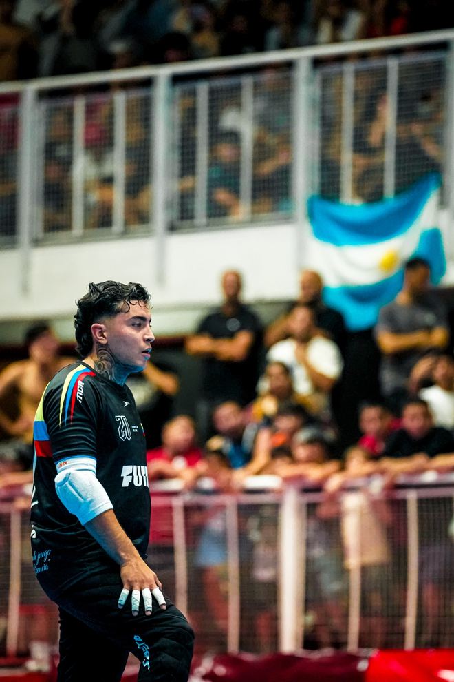 Un jugador de Colombia se agacha en la banda con una bandera argentina desplegada en la tribuna detrás