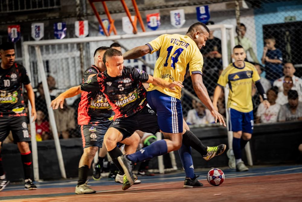 Dos jugadores se pelean el balón cuerpo a cuerpo, con el público pegado a la reja